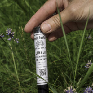 hand holding a tube of rolled joints in a bush of lavender